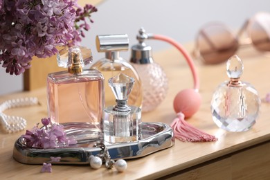 Photo of Bottles of perfumes, accessories and lilac flowers on wooden table, closeup