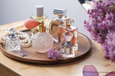 Photo of Bottles of perfumes, accessories and lilac flowers on wooden table