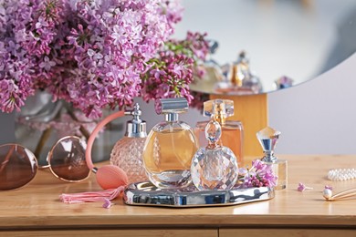 Photo of Bottles of perfumes, accessories and lilac flowers on wooden table