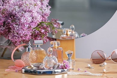Photo of Bottles of perfumes, accessories and lilac flowers on wooden table