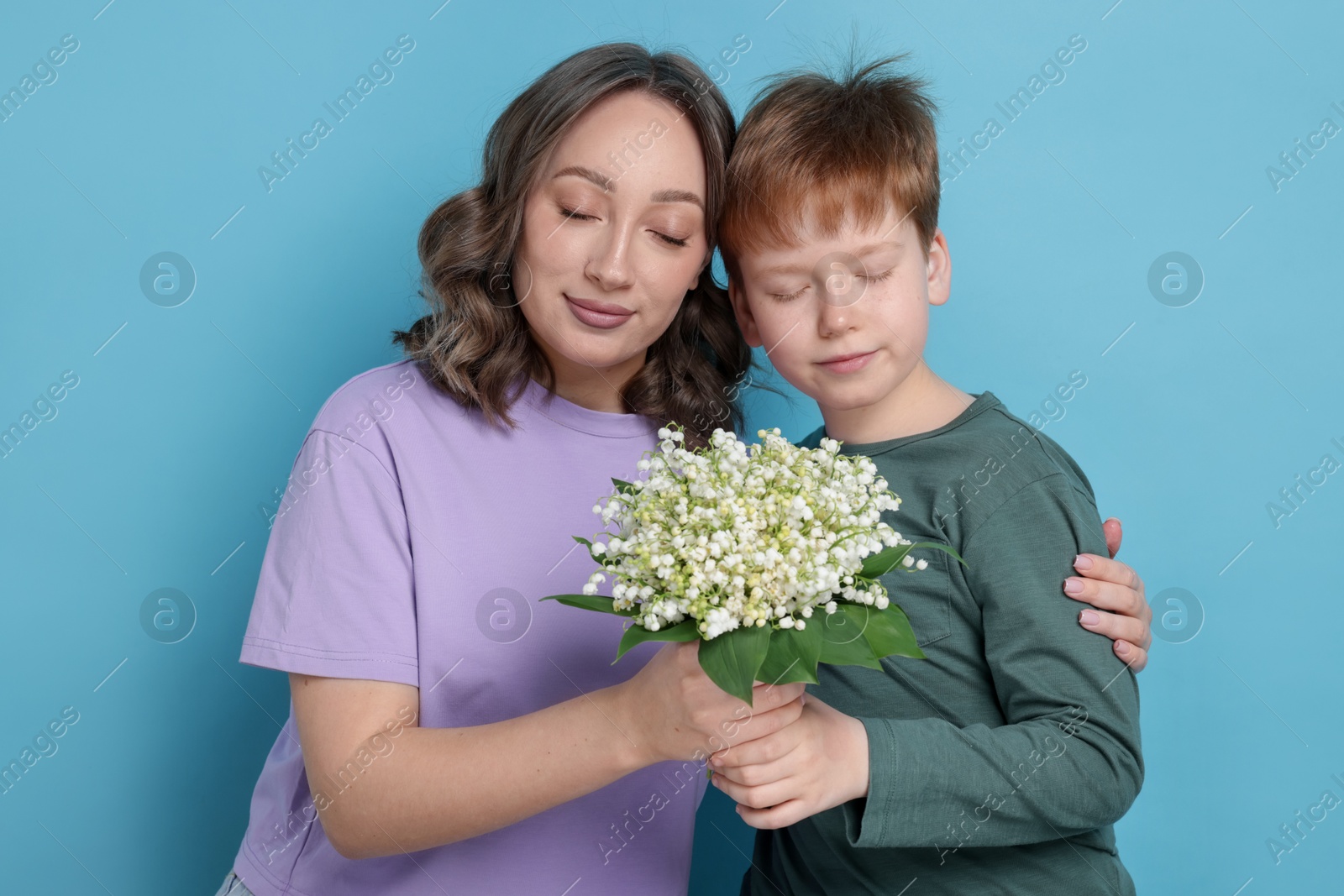 Boy giving his mother beautiful bouquet of lily-of-the-valley flowers on light blue background Photo of Boy giving his mother beautiful bouquet of lily-of-the-valley flowers on light blue background