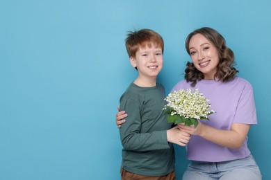 Photo of Boy giving his mother beautiful bouquet of lily-of-the-valley flowers on light blue background. Space for text