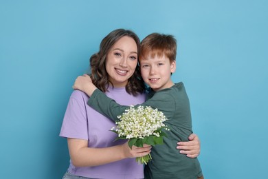 Photo of Boy giving his mother beautiful bouquet of lily-of-the-valley flowers on light blue background