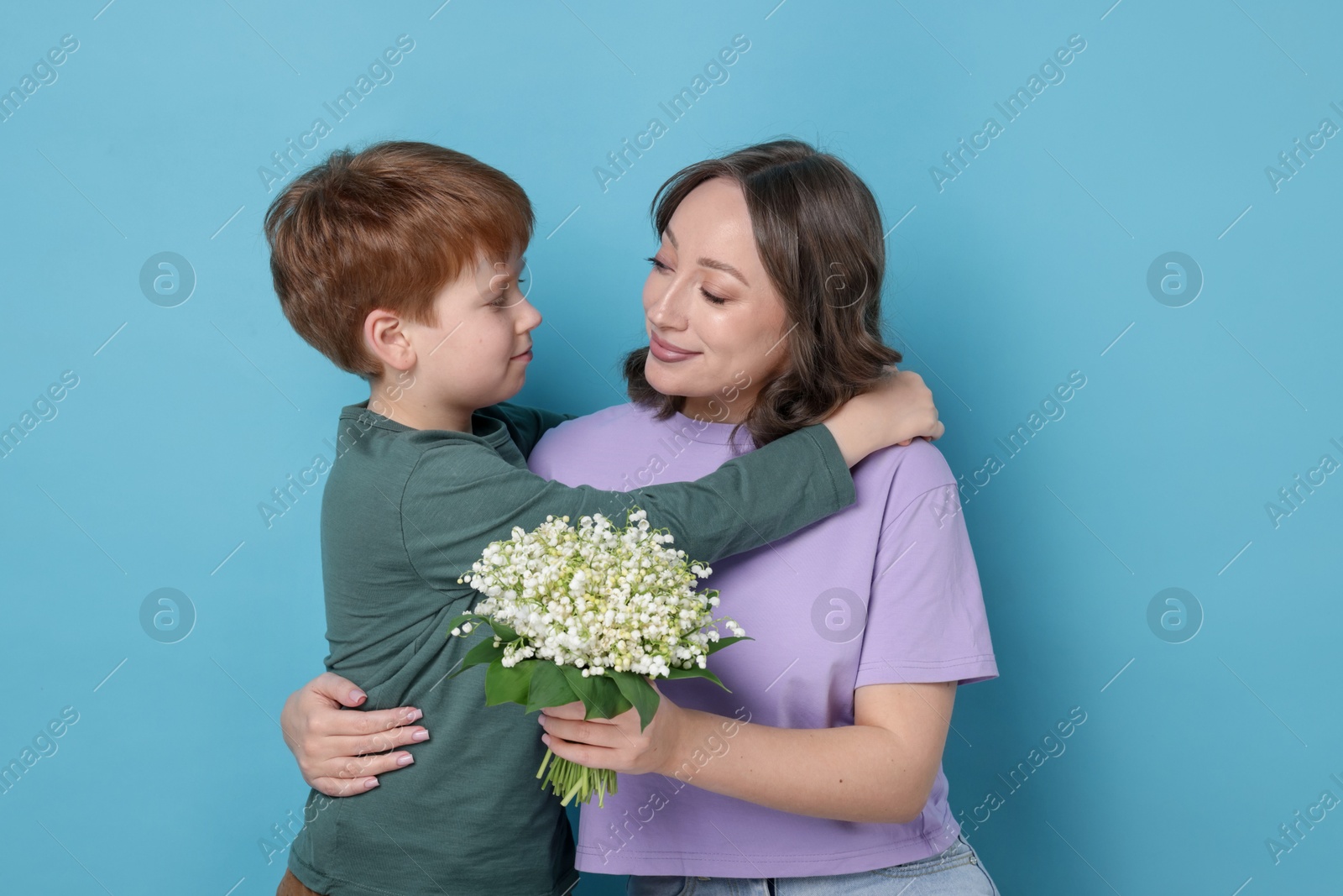 Boy giving his mother beautiful bouquet of lily-of-the-valley flowers on light blue background Photo of Boy giving his mother beautiful bouquet of lily-of-the-valley flowers on light blue background