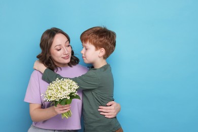 Photo of Boy giving his mother beautiful bouquet of lily-of-the-valley flowers on light blue background