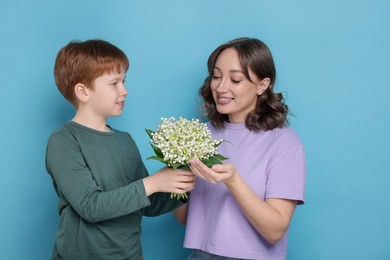Photo of Boy giving his mother beautiful bouquet of lily-of-the-valley flowers on light blue background