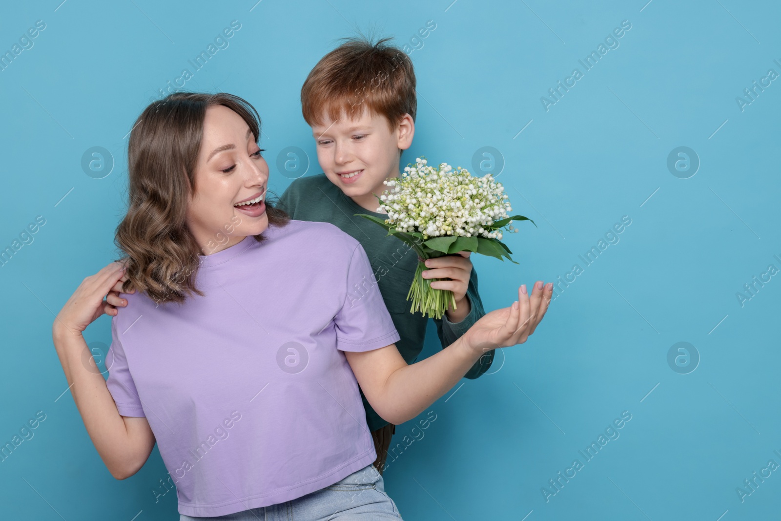 Boy surprising his mother with beautiful bouquet of lily-of-the-valley flowers on light blue background. Space for text Photo of Boy surprising his mother with beautiful bouquet of lily-of-the-valley flowers on light blue background. Space for text
