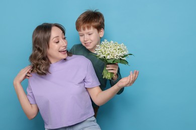 Photo of Boy surprising his mother with beautiful bouquet of lily-of-the-valley flowers on light blue background. Space for text