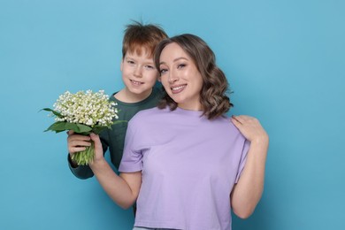 Photo of Boy giving his mother beautiful bouquet of lily-of-the-valley flowers on light blue background