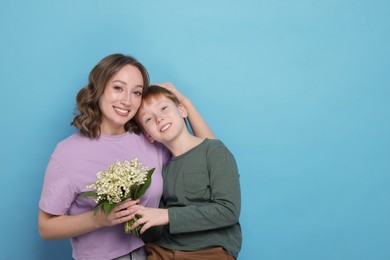 Photo of Boy giving his mother beautiful bouquet of lily-of-the-valley flowers on light blue background. Space for text