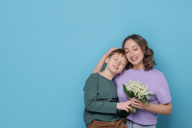Photo of Boy giving his mother beautiful bouquet of lily-of-the-valley flowers on light blue background. Space for text