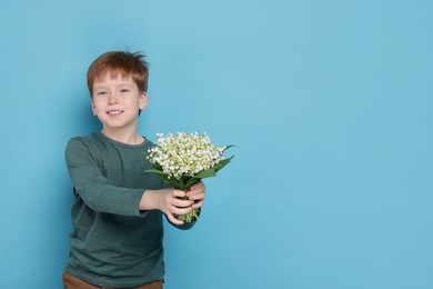 Photo of Boy with bouquet of beautiful lily-of-the-valley flowers on light blue background. Space for text