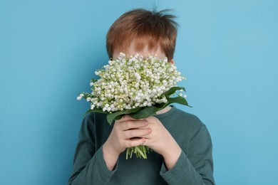 Photo of Boy with bouquet of beautiful lily-of-the-valley flowers on light blue background