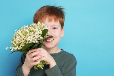 Photo of Boy with bouquet of beautiful lily-of-the-valley flowers on light blue background