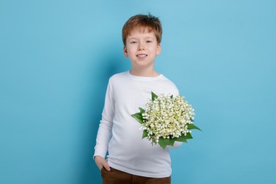 Photo of Boy with bouquet of beautiful lily-of-the-valley flowers on light blue background