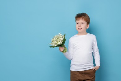 Photo of Boy with bouquet of beautiful lily-of-the-valley flowers on light blue background. Space for text