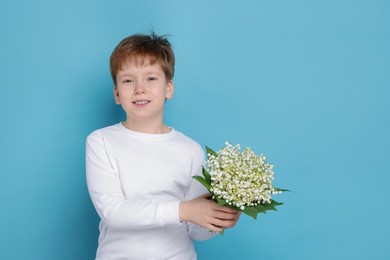 Photo of Boy with bouquet of beautiful lily-of-the-valley flowers on light blue background