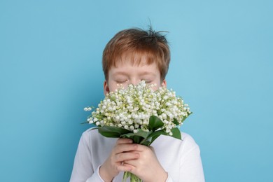 Photo of Boy with bouquet of beautiful lily-of-the-valley flowers on light blue background