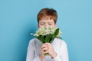 Photo of Boy with bouquet of beautiful lily-of-the-valley flowers on light blue background