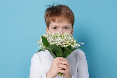 Photo of Boy with bouquet of beautiful lily-of-the-valley flowers on light blue background
