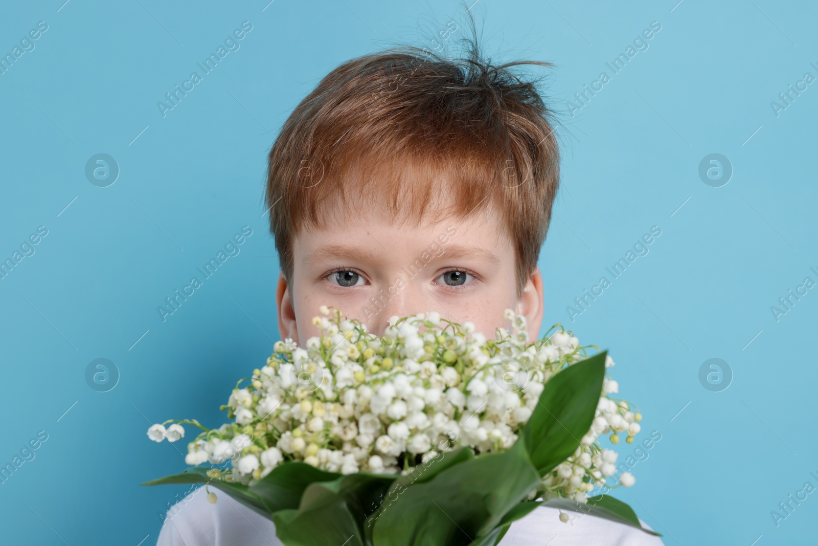 Boy with bouquet of beautiful lily-of-the-valley flowers on light blue background Photo of Boy with bouquet of beautiful lily-of-the-valley flowers on light blue background