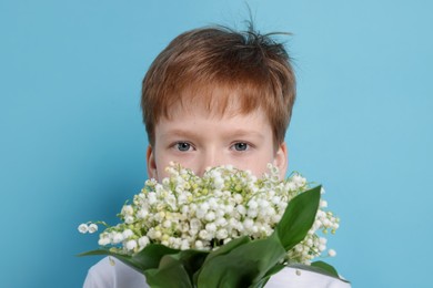 Photo of Boy with bouquet of beautiful lily-of-the-valley flowers on light blue background