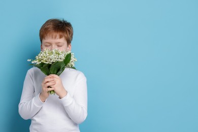 Photo of Boy with bouquet of beautiful lily-of-the-valley flowers on light blue background. Space for text