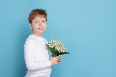Photo of Boy with bouquet of beautiful lily-of-the-valley flowers on light blue background. Space for text