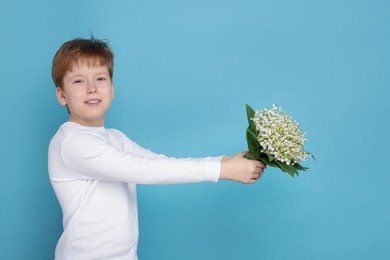 Photo of Boy with bouquet of beautiful lily-of-the-valley flowers on light blue background