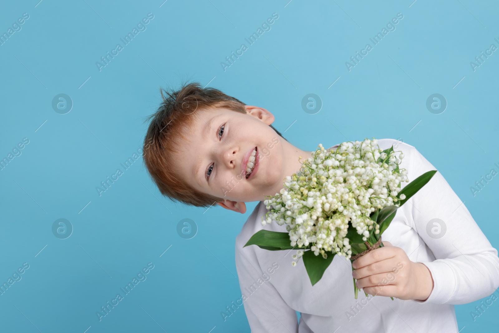 Boy with bouquet of beautiful lily-of-the-valley flowers on light blue background Photo of Boy with bouquet of beautiful lily-of-the-valley flowers on light blue background