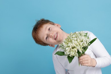 Photo of Boy with bouquet of beautiful lily-of-the-valley flowers on light blue background
