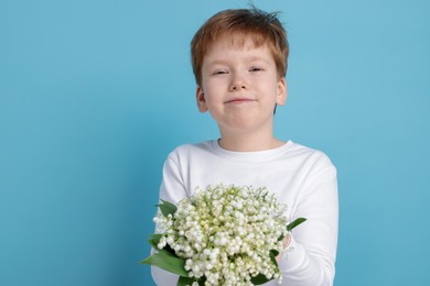Photo of Boy with bouquet of beautiful lily-of-the-valley flowers on light blue background