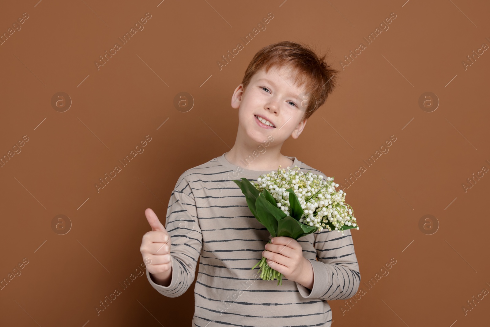 Boy with bouquet of beautiful lily-of-the-valley flowers showing thumbs up on brown background Photo of Boy with bouquet of beautiful lily-of-the-valley flowers showing thumbs up on brown background