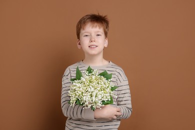 Photo of Boy with bouquet of beautiful lily-of-the-valley flowers on brown background