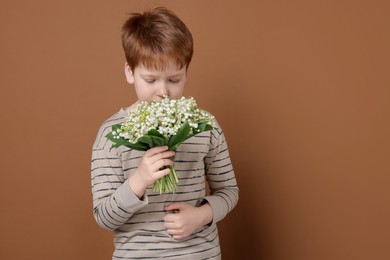 Photo of Boy with bouquet of beautiful lily-of-the-valley flowers on brown background