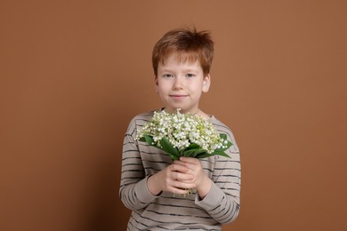 Photo of Boy with bouquet of beautiful lily-of-the-valley flowers on brown background