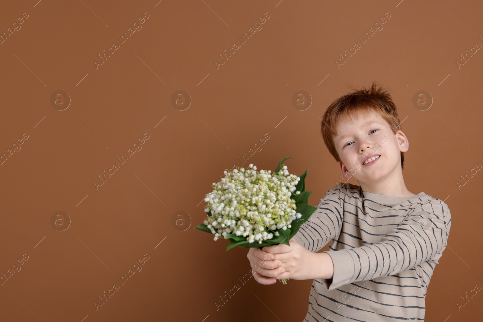 Boy with bouquet of beautiful lily-of-the-valley flowers on brown background. Space for text Photo of Boy with bouquet of beautiful lily-of-the-valley flowers on brown background. Space for text
