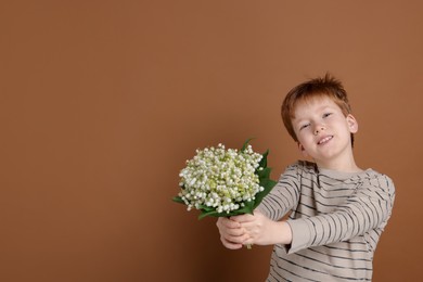 Photo of Boy with bouquet of beautiful lily-of-the-valley flowers on brown background. Space for text