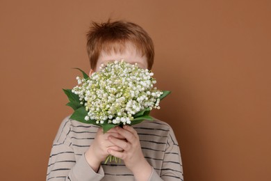 Photo of Boy with bouquet of beautiful lily-of-the-valley flowers on brown background
