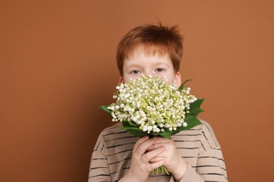 Photo of Boy with bouquet of beautiful lily-of-the-valley flowers on brown background