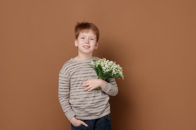 Photo of Boy with bouquet of beautiful lily-of-the-valley flowers on brown background