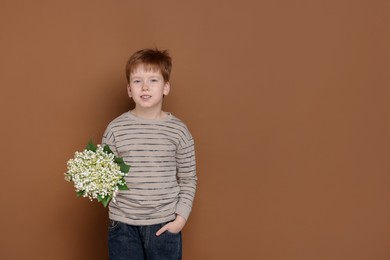 Photo of Boy with bouquet of beautiful lily-of-the-valley flowers on brown background. Space for text