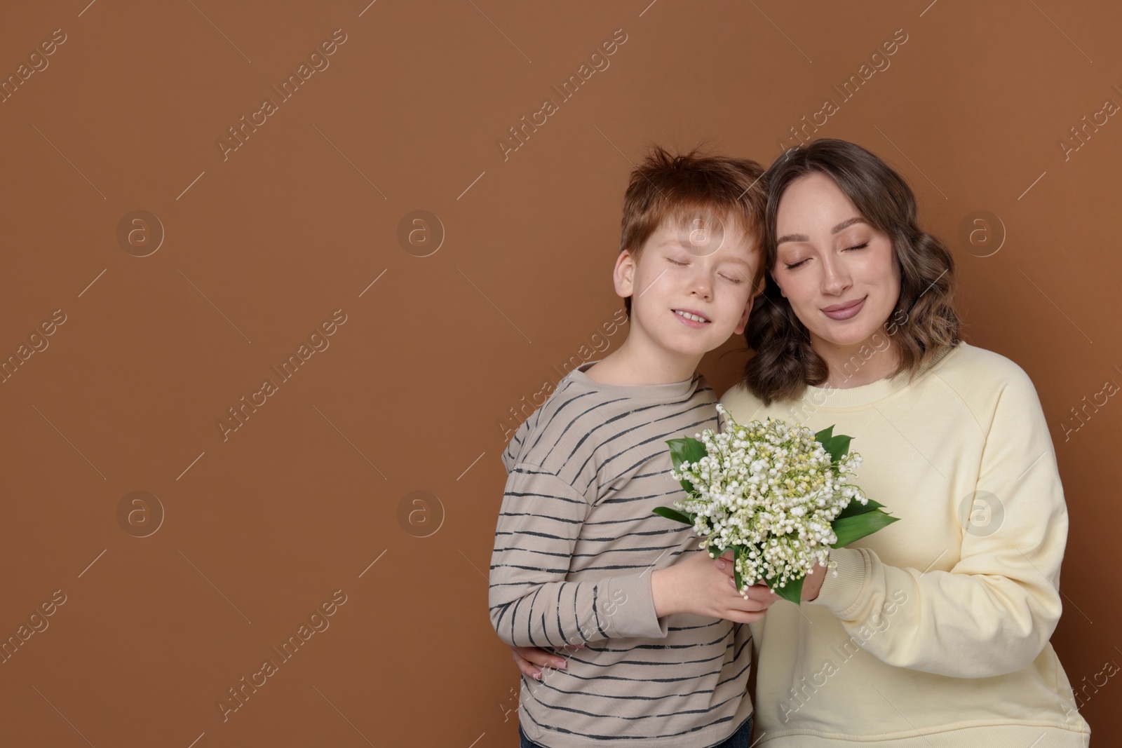 Boy giving his mother beautiful bouquet of lily-of-the-valley flowers on brown background. Space for text Photo of Boy giving his mother beautiful bouquet of lily-of-the-valley flowers on brown background. Space for text