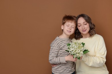 Photo of Boy giving his mother beautiful bouquet of lily-of-the-valley flowers on brown background. Space for text