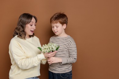 Photo of Boy giving his mother beautiful bouquet of lily-of-the-valley flowers on brown background. Space for text