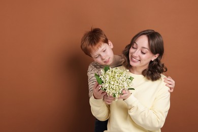 Photo of Boy giving his mother beautiful bouquet of lily-of-the-valley flowers on brown background. Space for text