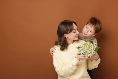 Photo of Boy giving his mother beautiful bouquet of lily-of-the-valley flowers on brown background. Space for text