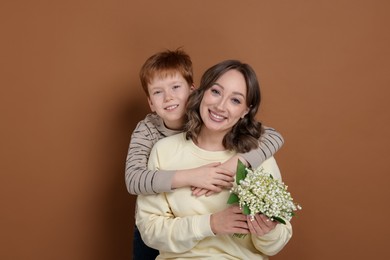 Photo of Boy giving his mother beautiful bouquet of lily-of-the-valley flowers on brown background