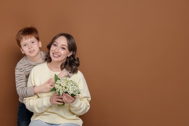 Photo of Boy giving his mother beautiful bouquet of lily-of-the-valley flowers on brown background. Space for text