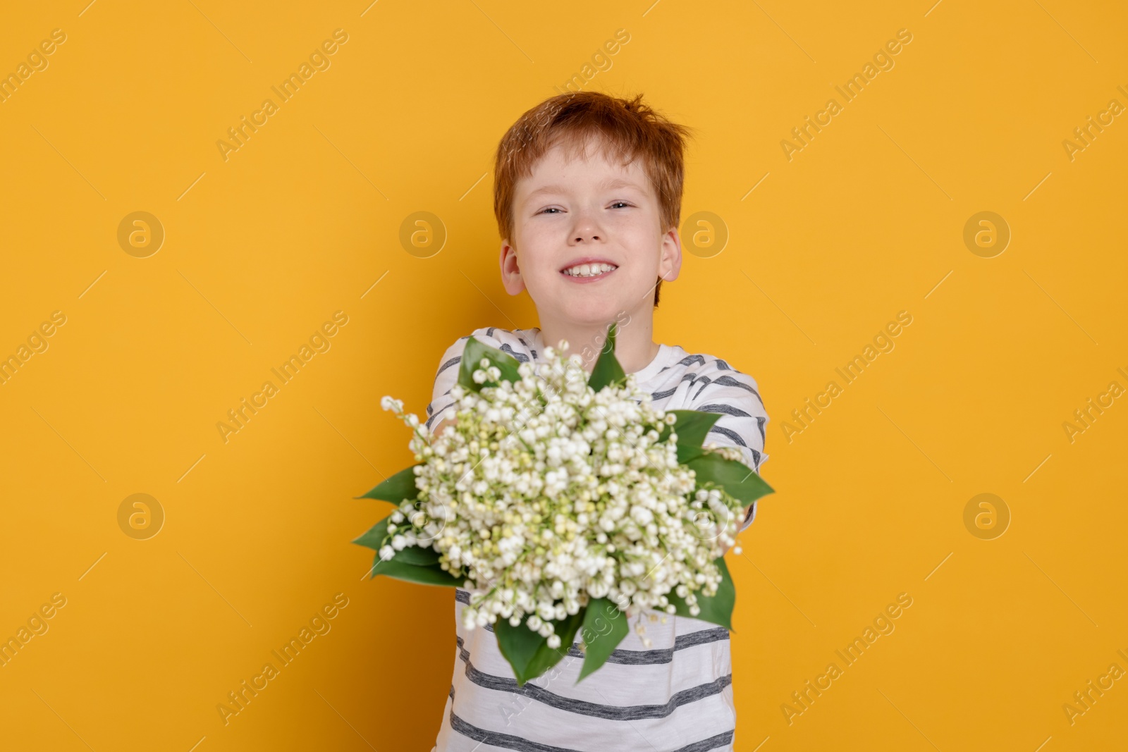 Boy with bouquet of beautiful lily-of-the-valley flowers on yellow background Photo of Boy with bouquet of beautiful lily-of-the-valley flowers on yellow background